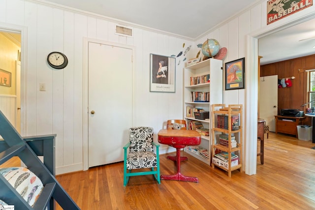 living area featuring ornamental molding, a decorative wall, wood finished floors, and wood walls