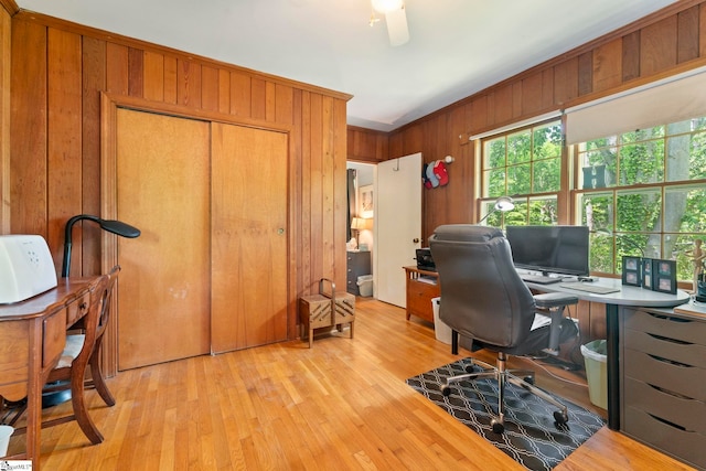 office featuring wooden walls, light wood-style floors, and a ceiling fan