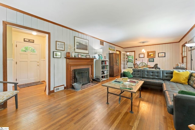 living room featuring visible vents, crown molding, a brick fireplace, wood walls, and wood-type flooring