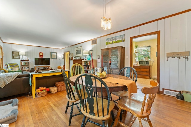 dining space with wood walls, ornamental molding, wood finished floors, and visible vents