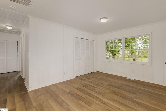 empty room featuring visible vents, ornamental molding, baseboards, and wood finished floors