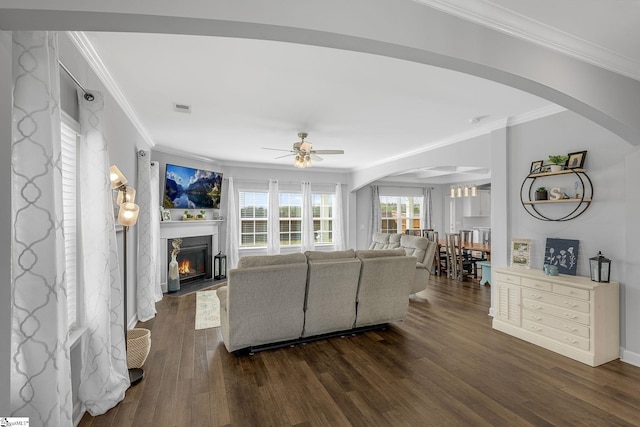 living room with crown molding, arched walkways, dark wood-style floors, and a fireplace with flush hearth