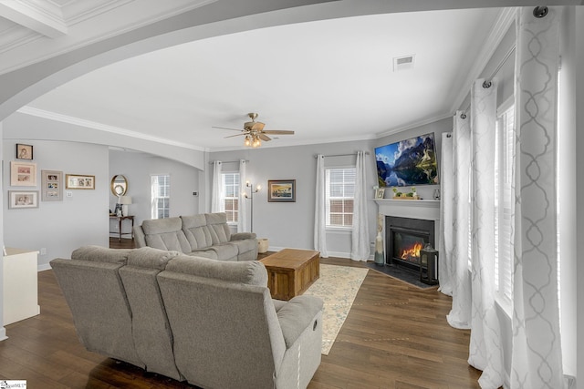 living area with dark wood-style flooring, arched walkways, visible vents, and a fireplace with flush hearth