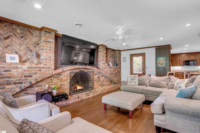 living room with recessed lighting, ceiling fan, crown molding, wood finished floors, and a fireplace