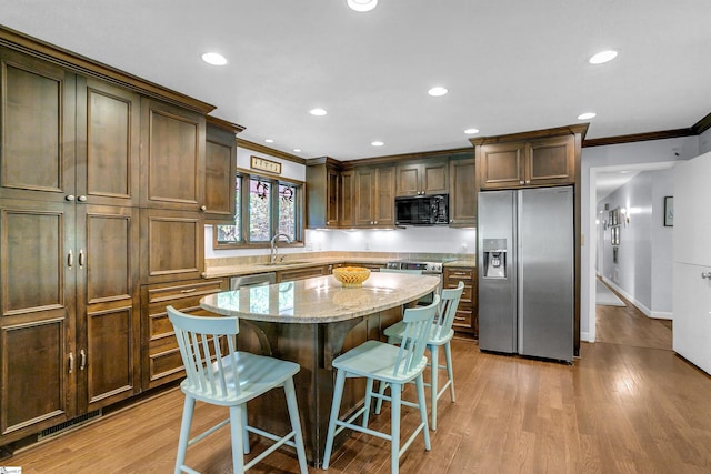 kitchen with light stone countertops, a center island, a kitchen bar, crown molding, and appliances with stainless steel finishes