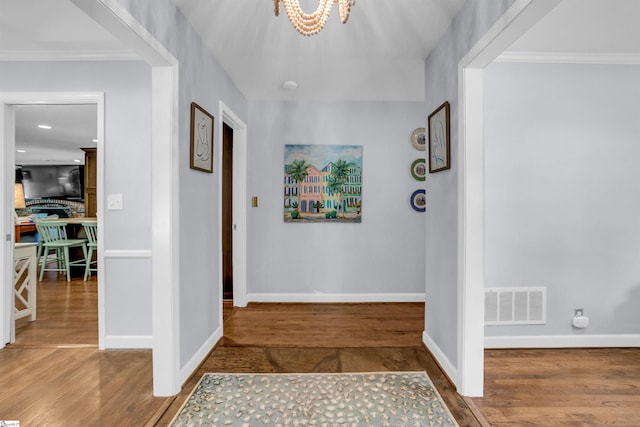 entryway with wood finished floors, visible vents, baseboards, a chandelier, and ornamental molding