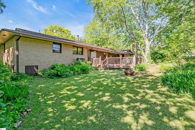 rear view of property with a lawn, a deck, and brick siding