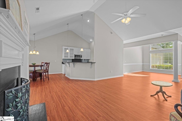living room with wood finished floors, ceiling fan with notable chandelier, high vaulted ceiling, a fireplace, and baseboards