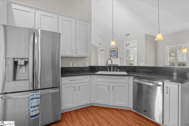 kitchen with light wood-style flooring, a sink, pendant lighting, white cabinets, and appliances with stainless steel finishes