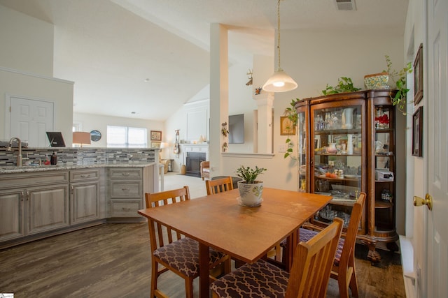 dining room with a fireplace, lofted ceiling, dark wood-type flooring, and visible vents