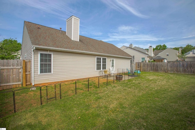 back of property with a fenced backyard, roof with shingles, a chimney, and a yard