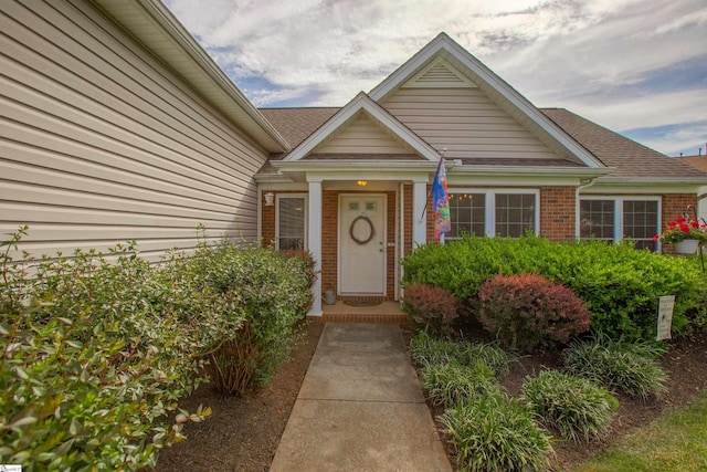 doorway to property featuring a shingled roof and brick siding