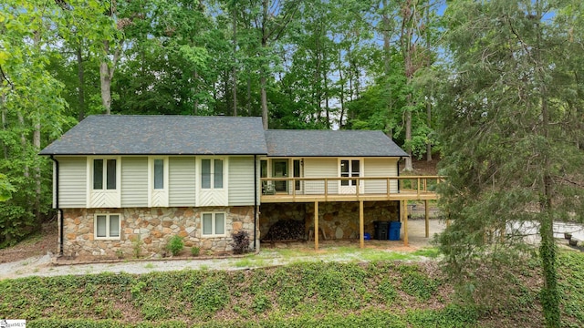 rear view of house with stone siding, a wooden deck, and a shingled roof
