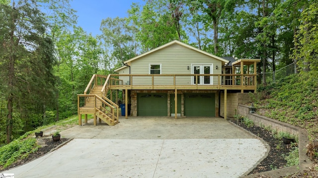 back of property featuring french doors, a garage, concrete driveway, stairway, and a wooden deck