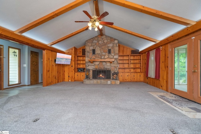 unfurnished living room featuring wood walls, lofted ceiling with beams, carpet floors, a ceiling fan, and a stone fireplace