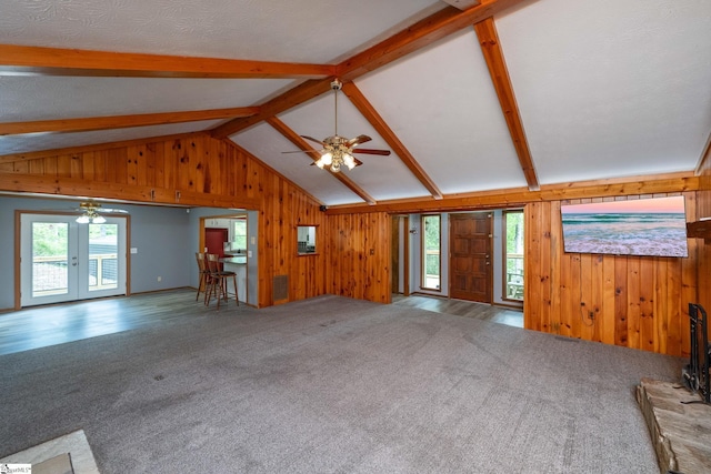 unfurnished living room featuring ceiling fan, wood walls, carpet flooring, and lofted ceiling with beams