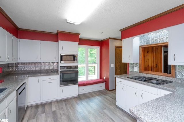 kitchen with black appliances, ornamental molding, light wood finished floors, and tasteful backsplash