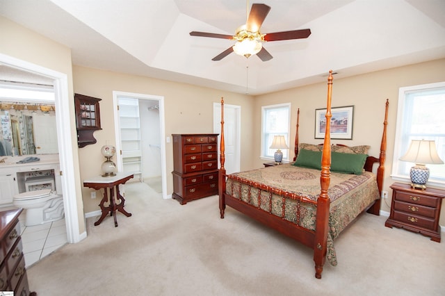 bedroom with a tray ceiling, baseboards, ensuite bathroom, a spacious closet, and light colored carpet