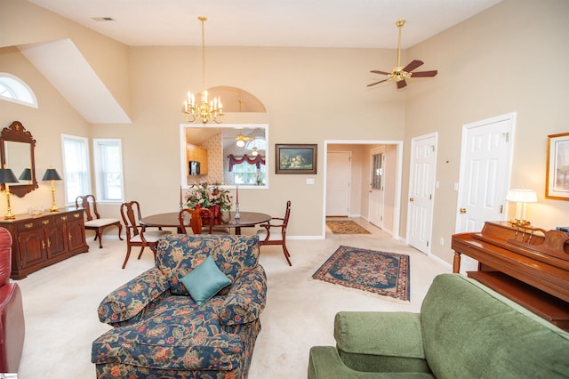 living room featuring baseboards, light carpet, high vaulted ceiling, and ceiling fan with notable chandelier
