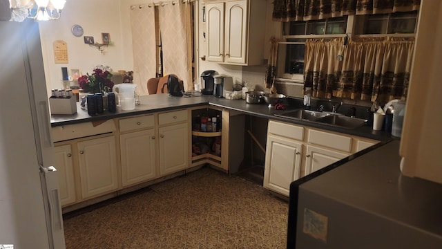 kitchen with a notable chandelier, dark countertops, cream cabinetry, and a sink