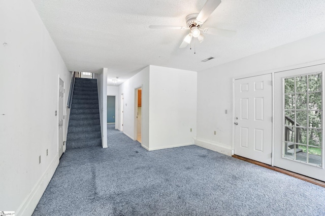 unfurnished living room with a textured ceiling, carpet flooring, visible vents, and stairs
