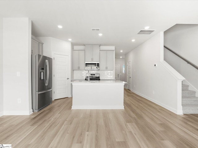 112 Arrow Ct, Greer, SC 29651 - kitchen with appliances with stainless steel finishes, light countertops, decorative backsplash, a kitchen island with sink, and light wood-style flooring