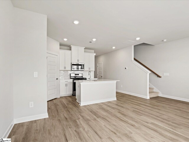 122 Arrow Ct, Greer, SC 29651 - kitchen with appliances with stainless steel finishes, light wood-style floors, white cabinetry, tasteful backsplash, and a center island with sink