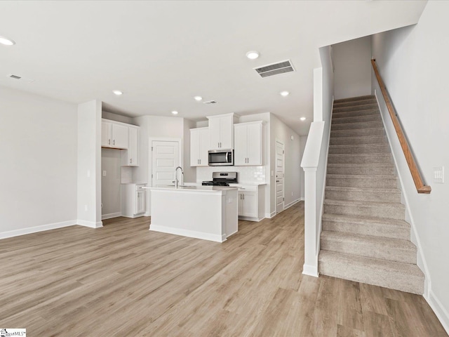 122 Arrow Ct, Greer, SC 29651 - kitchen with stainless steel microwave, range with gas cooktop, light wood-style flooring, white cabinetry, and an island with sink