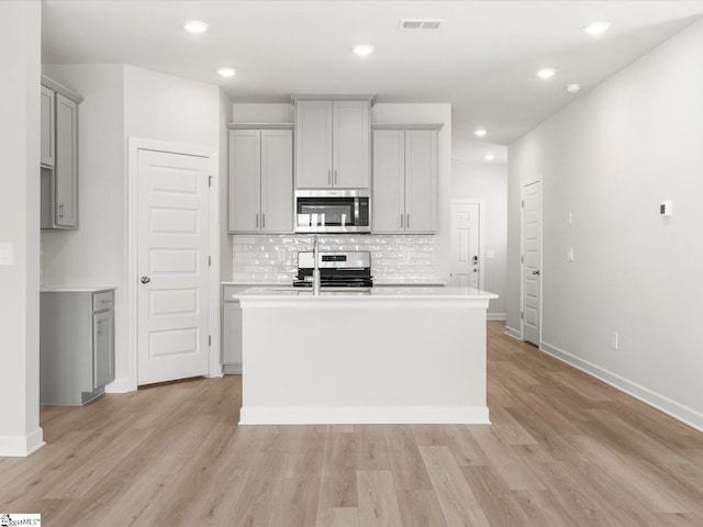 126 Arrow Ct, Greer, SC 29651 - kitchen featuring stainless steel appliances, gray cabinets, a kitchen island with sink, decorative backsplash, and light wood-type flooring