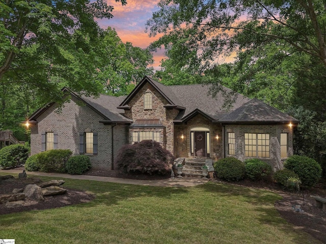 view of front facade with roof with shingles, stone siding, brick siding, and a front yard