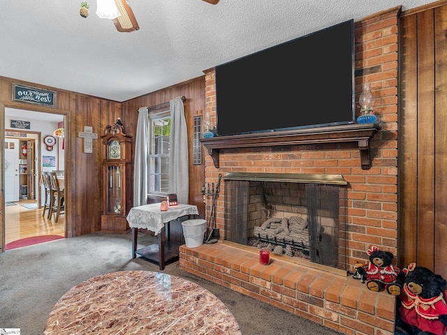 carpeted living room with wooden walls, a fireplace, ceiling fan, and a textured ceiling