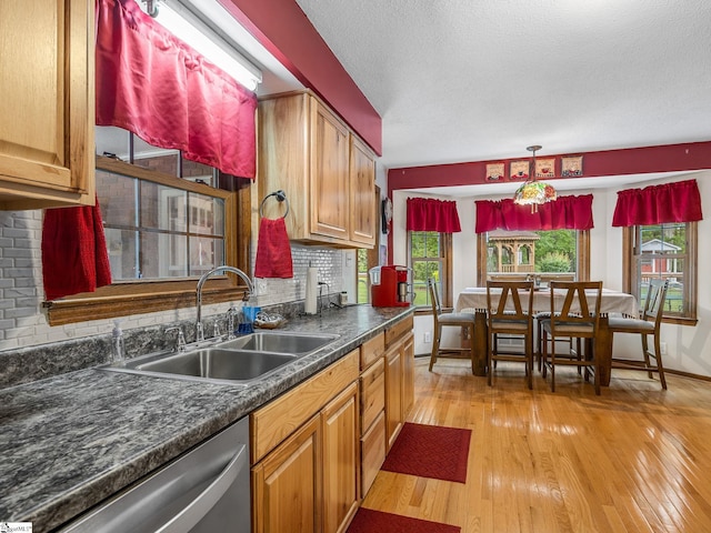 kitchen featuring light wood-style flooring, dishwasher, a sink, dark countertops, and tasteful backsplash