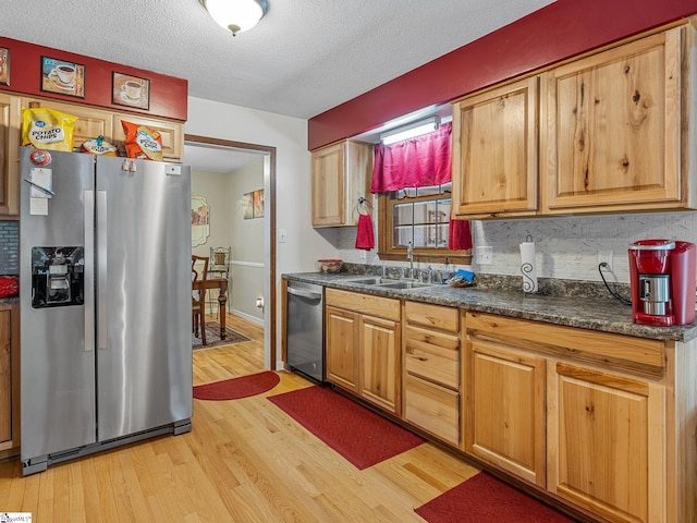 kitchen with light wood finished floors, a sink, dark countertops, tasteful backsplash, and appliances with stainless steel finishes