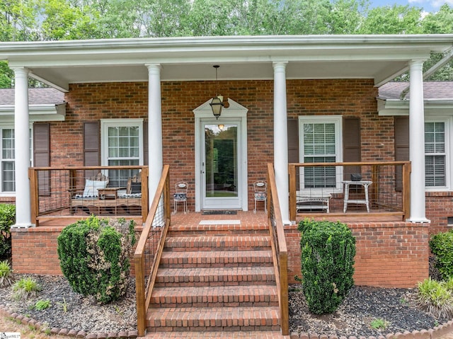 view of exterior entry featuring a porch and brick siding