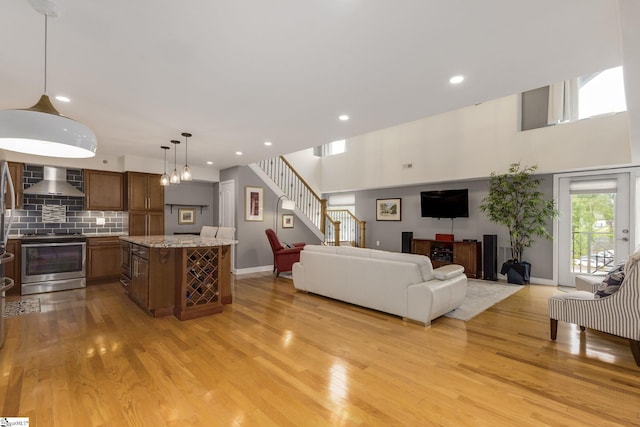 living room featuring light wood-type flooring, recessed lighting, stairway, a high ceiling, and baseboards