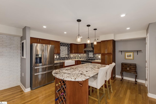 kitchen featuring a sink, light wood-type flooring, stainless steel appliances, and wall chimney range hood