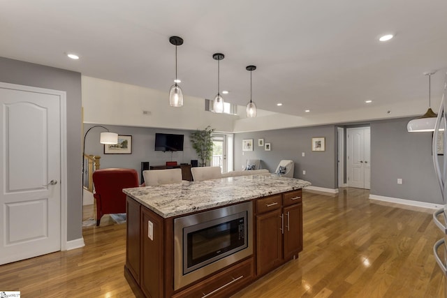 kitchen featuring a center island, pendant lighting, stainless steel microwave, baseboards, and light wood-style floors