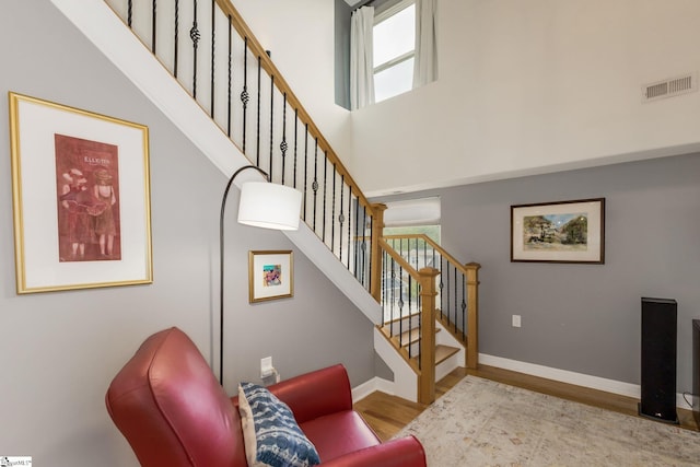 stairs featuring a wealth of natural light, visible vents, a high ceiling, and wood finished floors