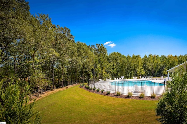 community pool featuring a wooded view, fence, and a lawn