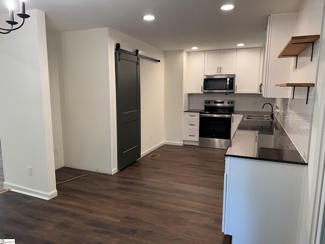 kitchen featuring a sink, open shelves, a barn door, dark countertops, and appliances with stainless steel finishes