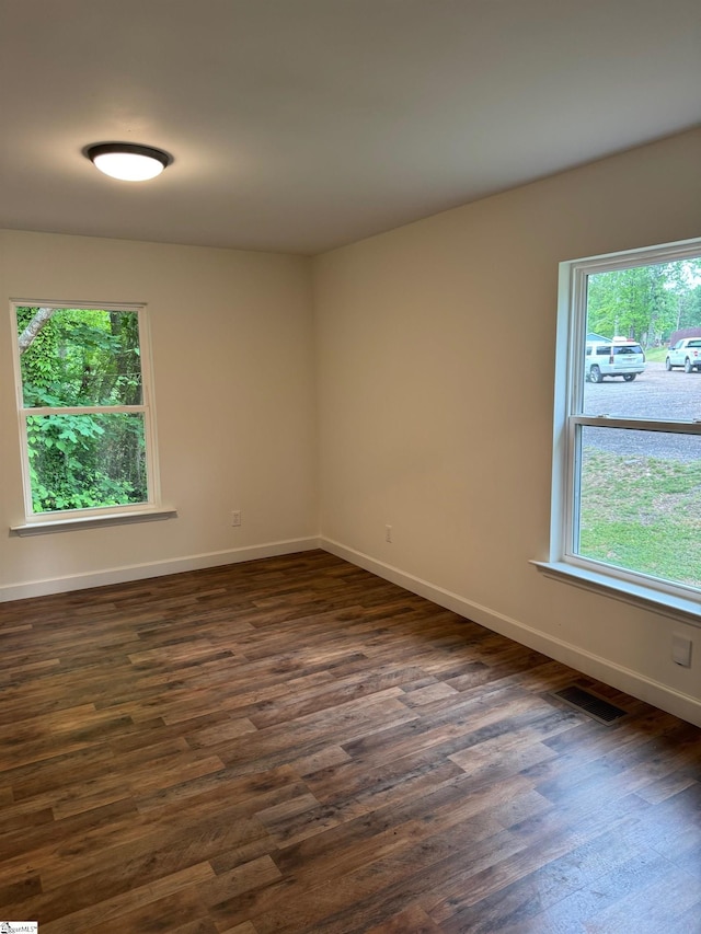 spare room with dark wood-style flooring, a wealth of natural light, baseboards, and visible vents