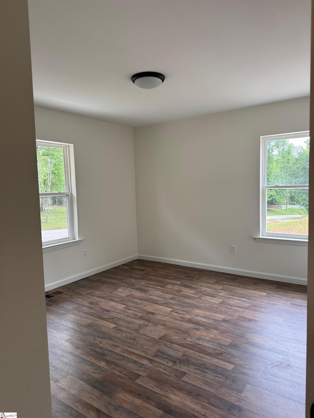 empty room with baseboards, dark wood-style flooring, and visible vents