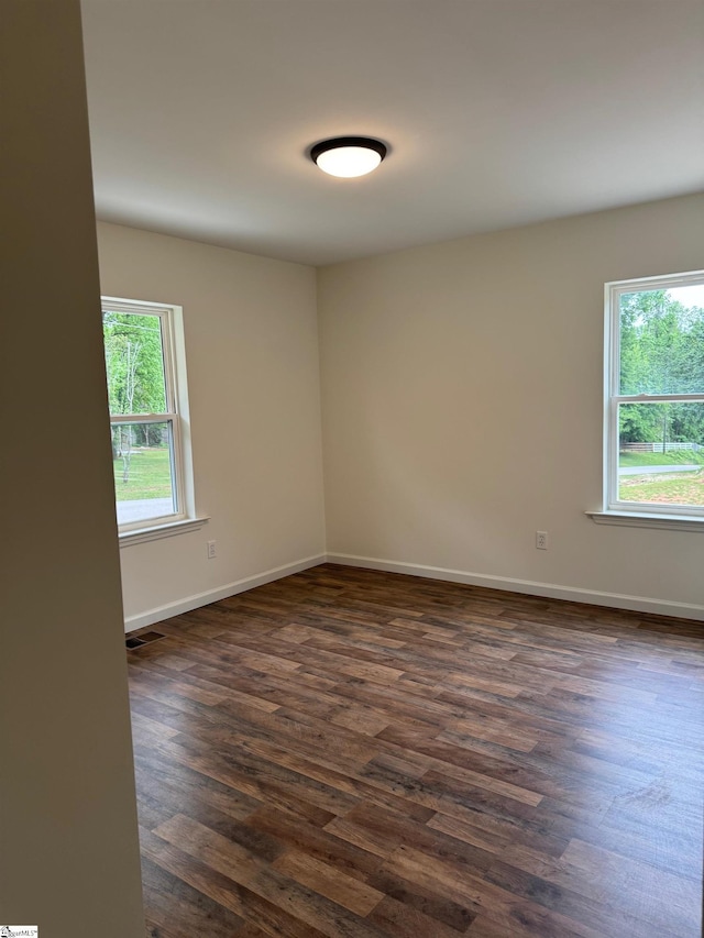 empty room with baseboards, a healthy amount of sunlight, and dark wood-style floors