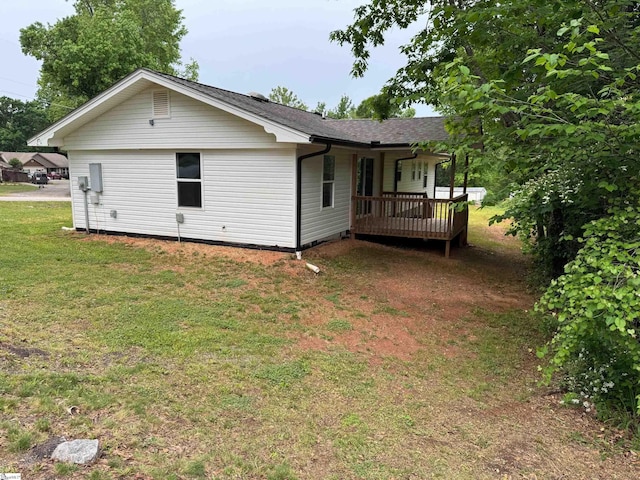 back of house with a deck, a shingled roof, and a lawn