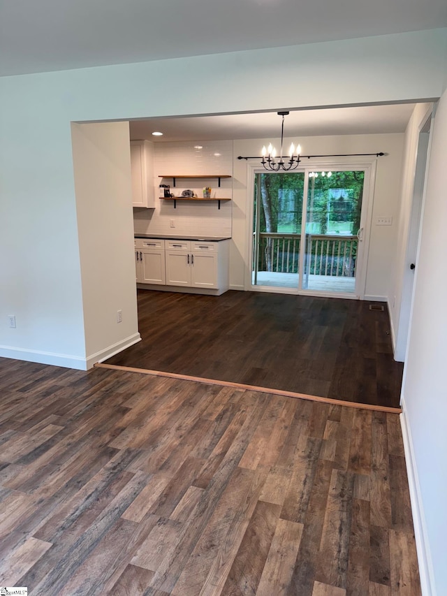 unfurnished dining area with an inviting chandelier, dark wood finished floors, and baseboards