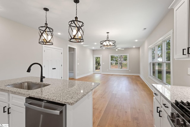 kitchen featuring light wood finished floors, a sink, pendant lighting, white cabinetry, and appliances with stainless steel finishes
