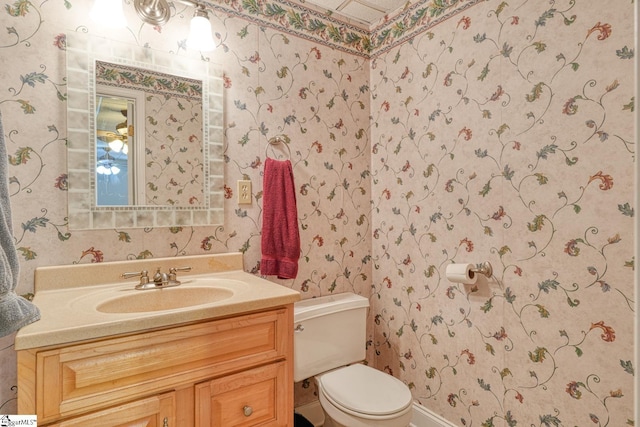bathroom with toilet, vanity, and wallpapered walls