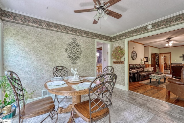 dining space featuring wood finished floors, wallpapered walls, a textured ceiling, ceiling fan, and ornamental molding