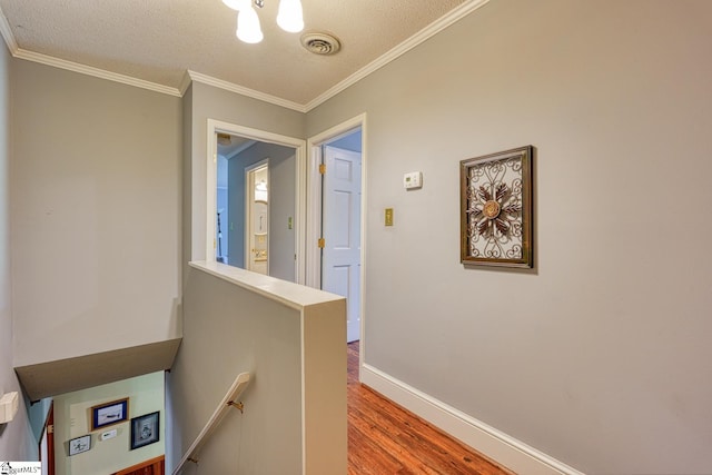 hall with a textured ceiling, visible vents, crown molding, wood finished floors, and an upstairs landing
