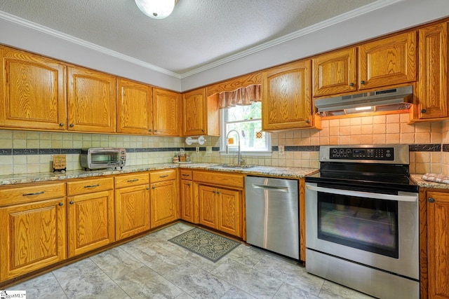 kitchen with a sink, brown cabinetry, under cabinet range hood, appliances with stainless steel finishes, and ornamental molding